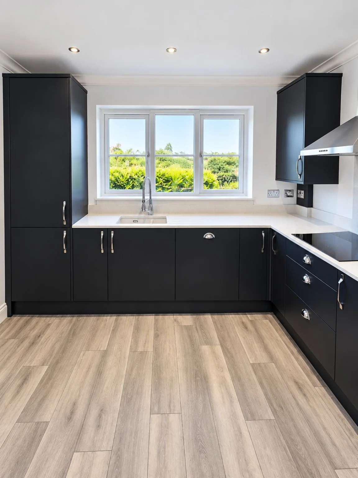 Dark fitted kitchen with sink run and wood-effect flooring by SM Installations